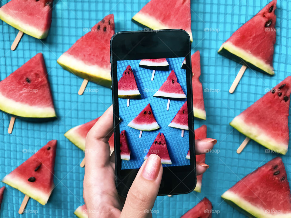 Female hand taking a photo of red watermelon slices for instagram 