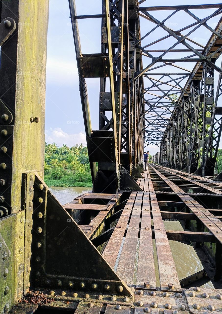 Bride and groom standing beside a man on the old railway bridge.