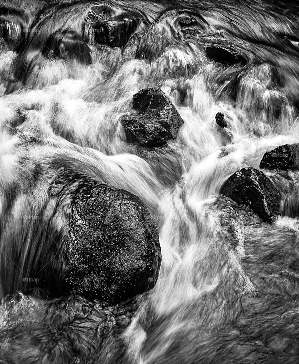 Fast flowing water over large rocks in black & white 