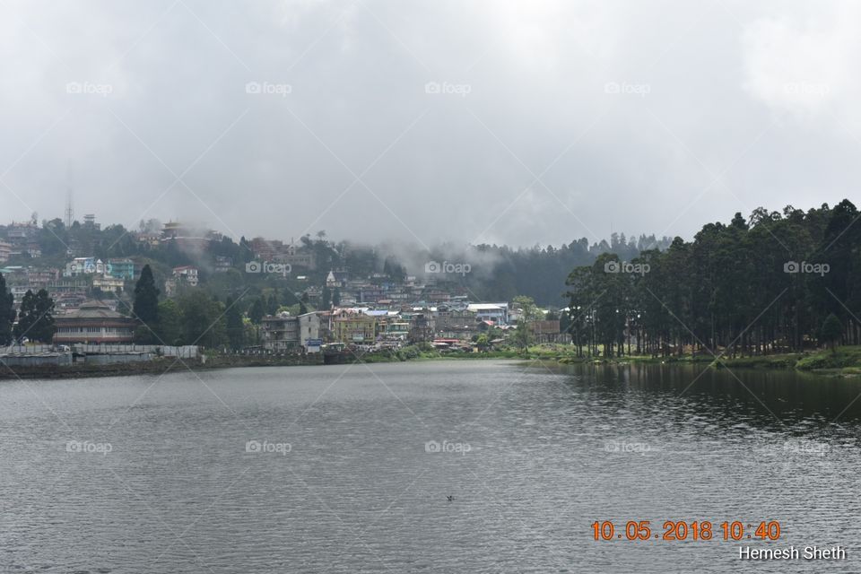 A beautiful lake, surrounded by trees and a small village beside. Clouds float nearby and have a boat ride in the lake, this is MIRIK Lake near Darjeeling, India.