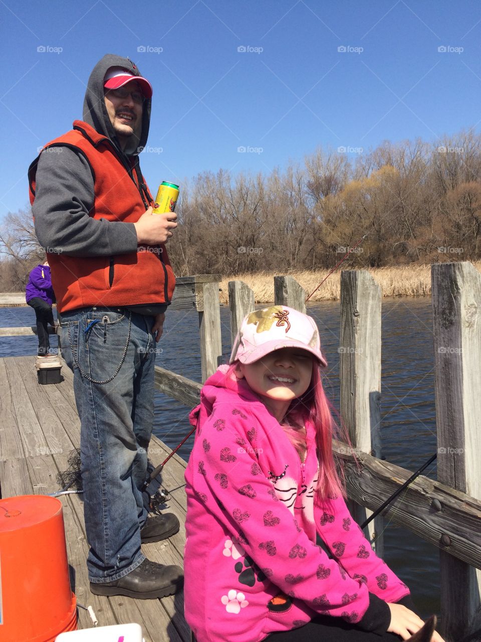 Father and daughter take a brief break from watching their fishing lines to smile for a pic from a dock on a lake in Minnesota. 