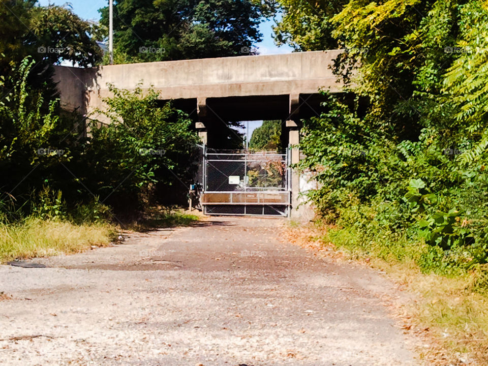 Unavailable Path. a gated off path under a railroad bridge.
