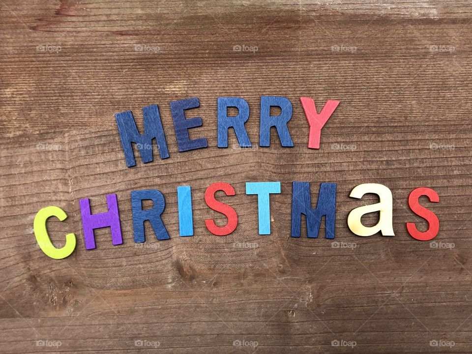 Merry Christmas text composed with colored wooden letters over a wooden board