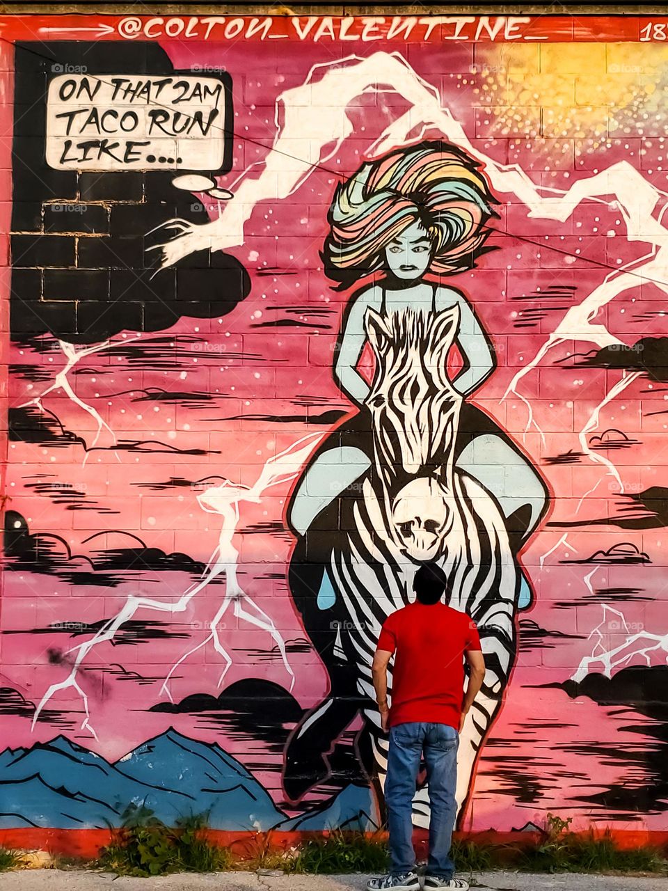 Man observing street art by Colton Vantine. On that 2AM taco run: a woman riding a zebra.  Tacos are a staple food in this city and often consumed late nights after a night out in the city.