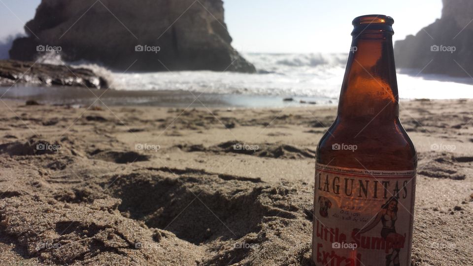 Lagunitas beer propped up in the sand in front of the ocean on a sunny beach