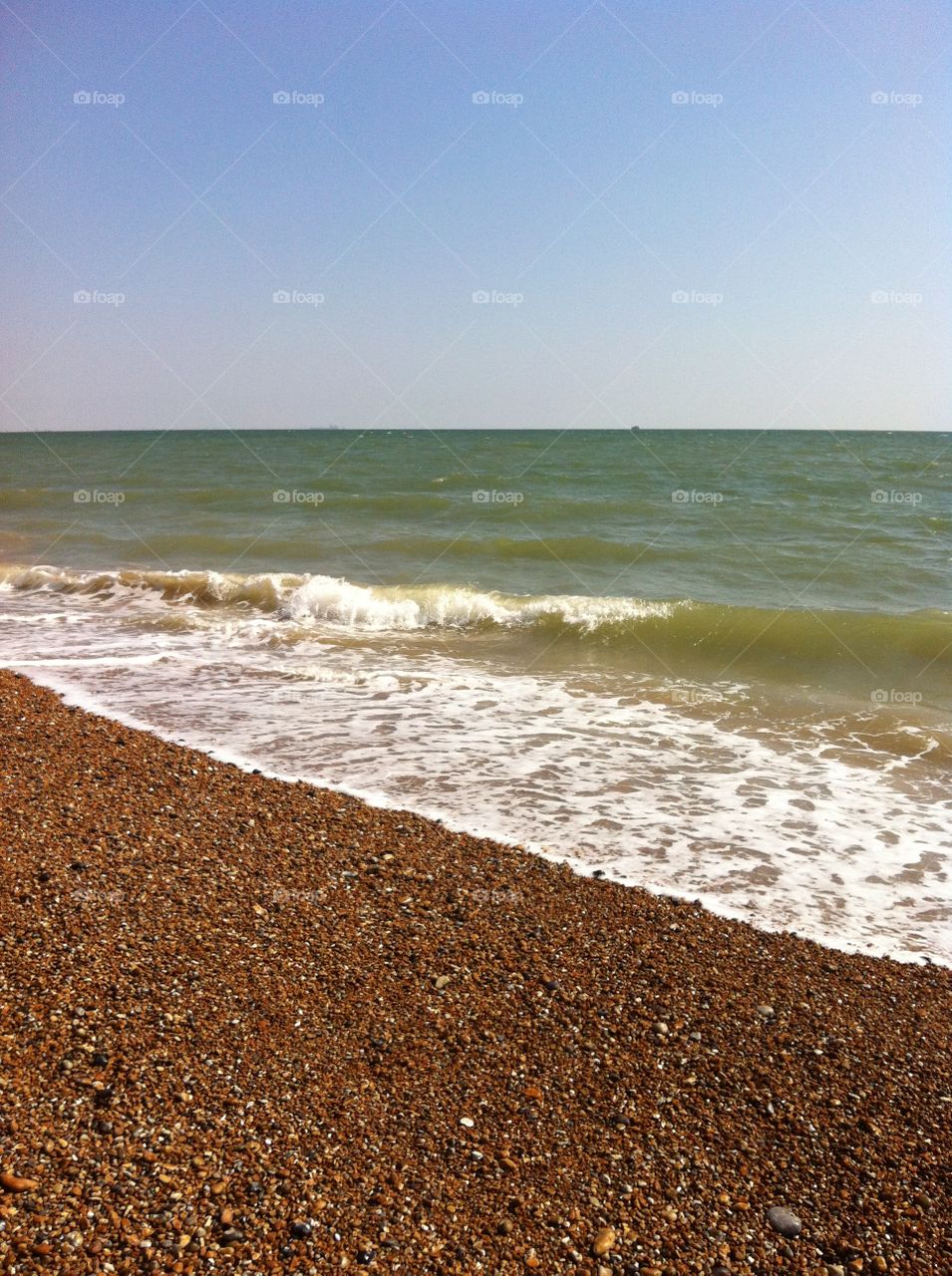 The sea waves roll in washing the stones on the beach, on a clear sunny day in Winchelsea, Sussex.
