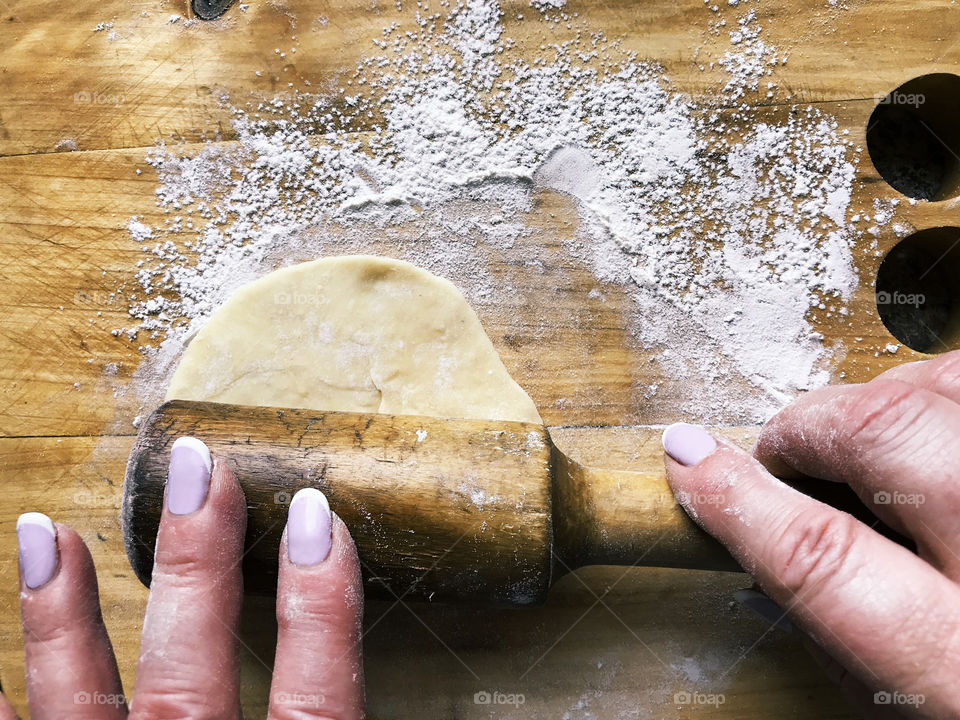 Hands of senior woman rolling out the dough on rustic wooden table with a flour 