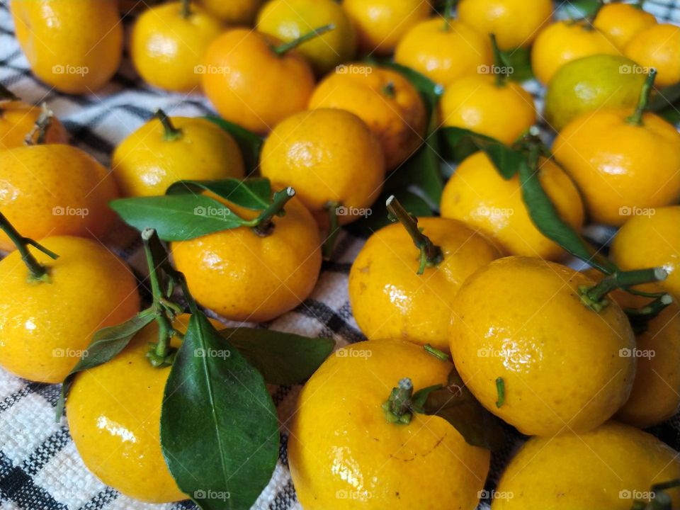 Fresh yellow orange fruits with leaves as background, top view
