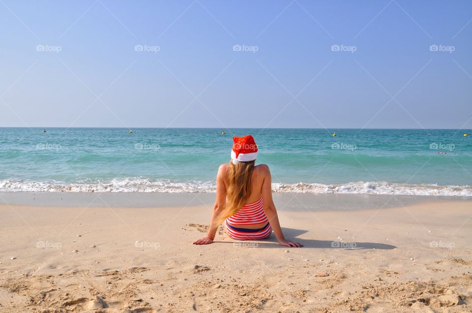 Woman in red santa hat sitting on kite beach during winter trip to dubai