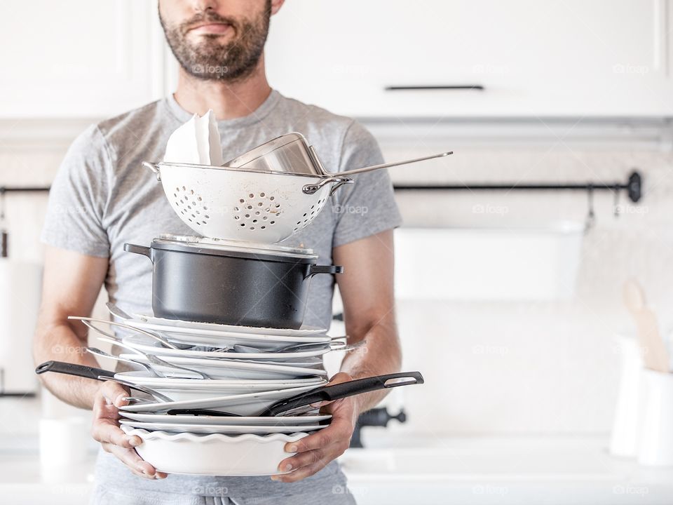 Bearded man is holding a lot of dirty dishes