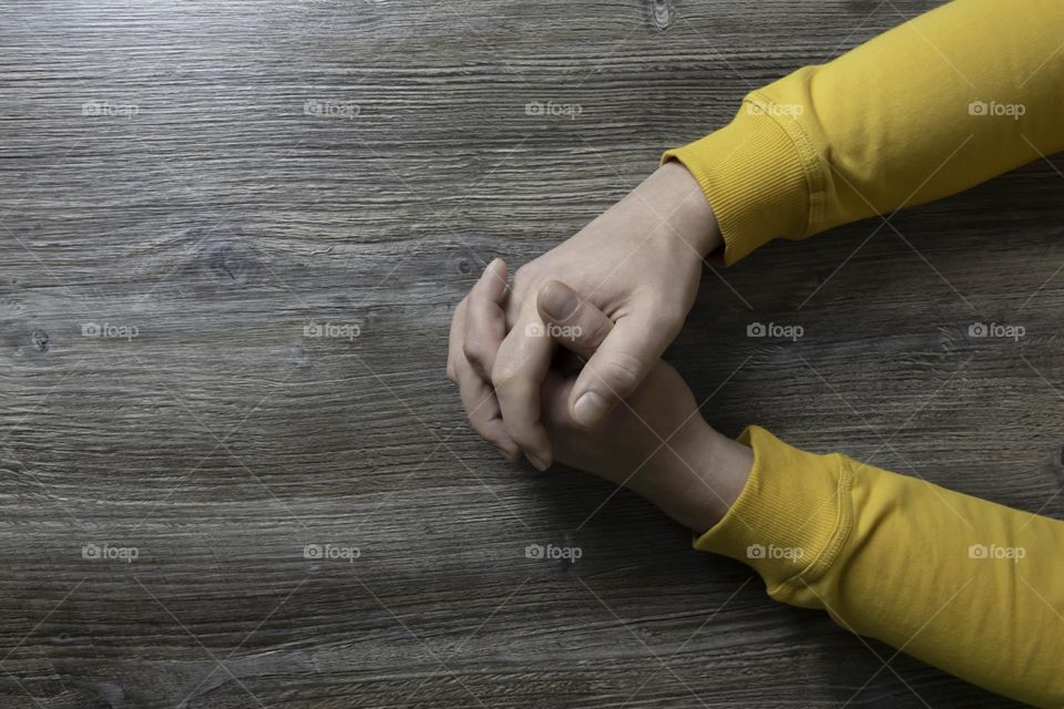 Men's hands in a yellow jacket lie on a gray wooden surface, which is used as a background or a surface with incident light.