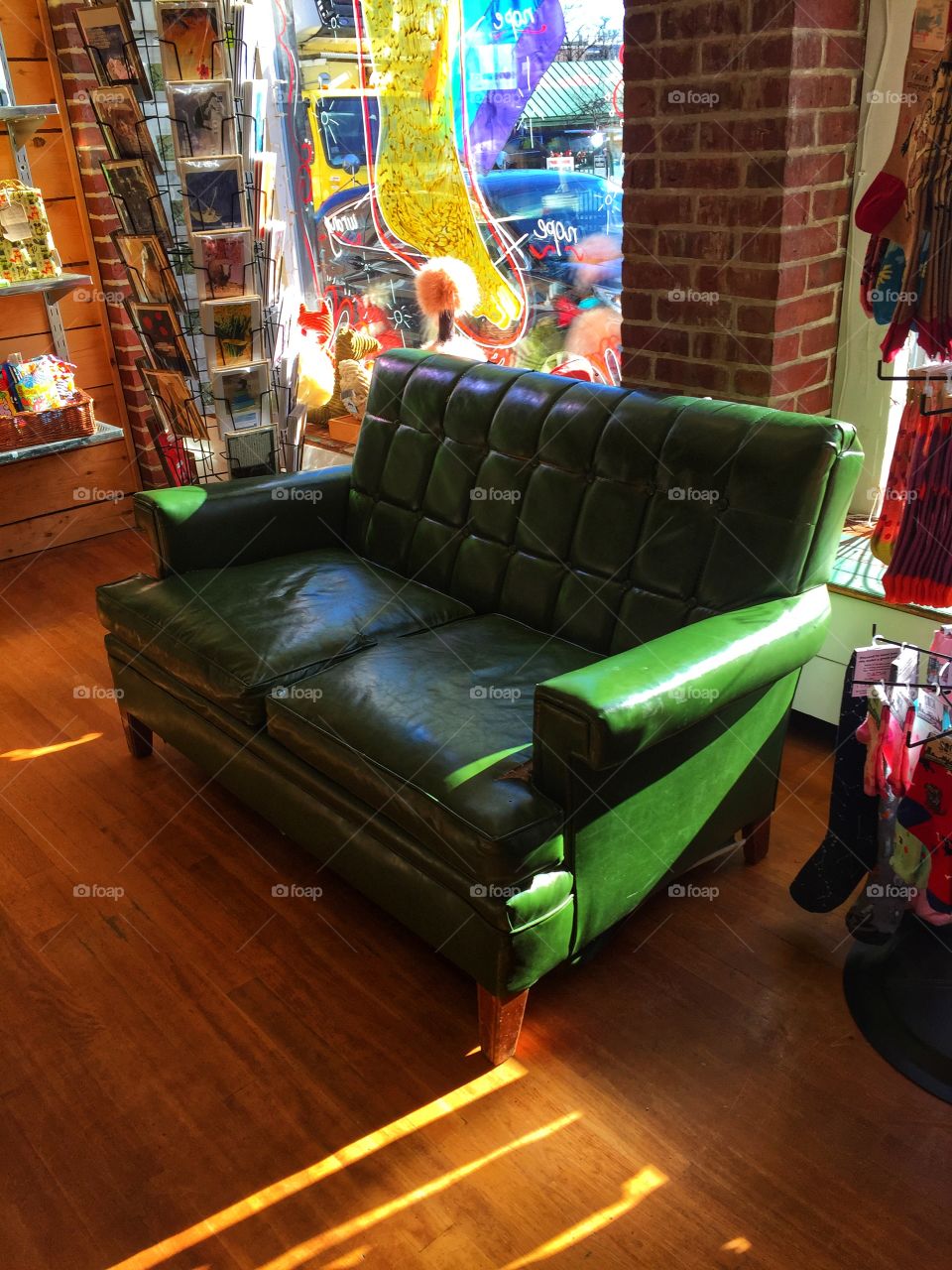 A green couch sits next to a window and a card display in a store. Afternoon light streams into the store from behind it.