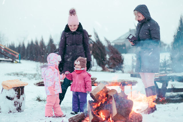 Family spending time together outdoors in the winter. Parents with children gathered around the campfire preparing marshmallows and snacks to toasting over the campfire using wooden sticks