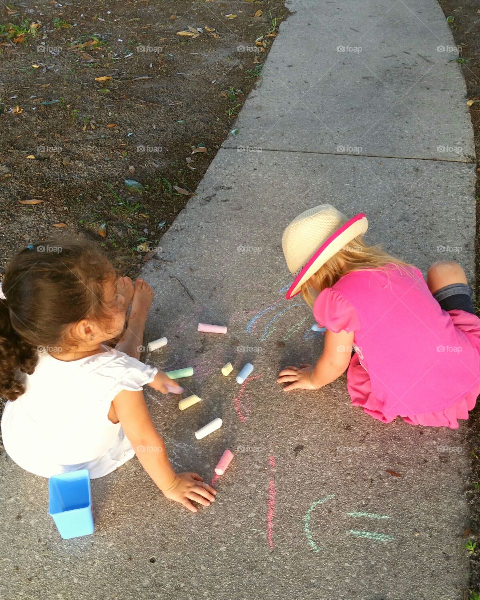 two little girls drawing  on the sidewalk
