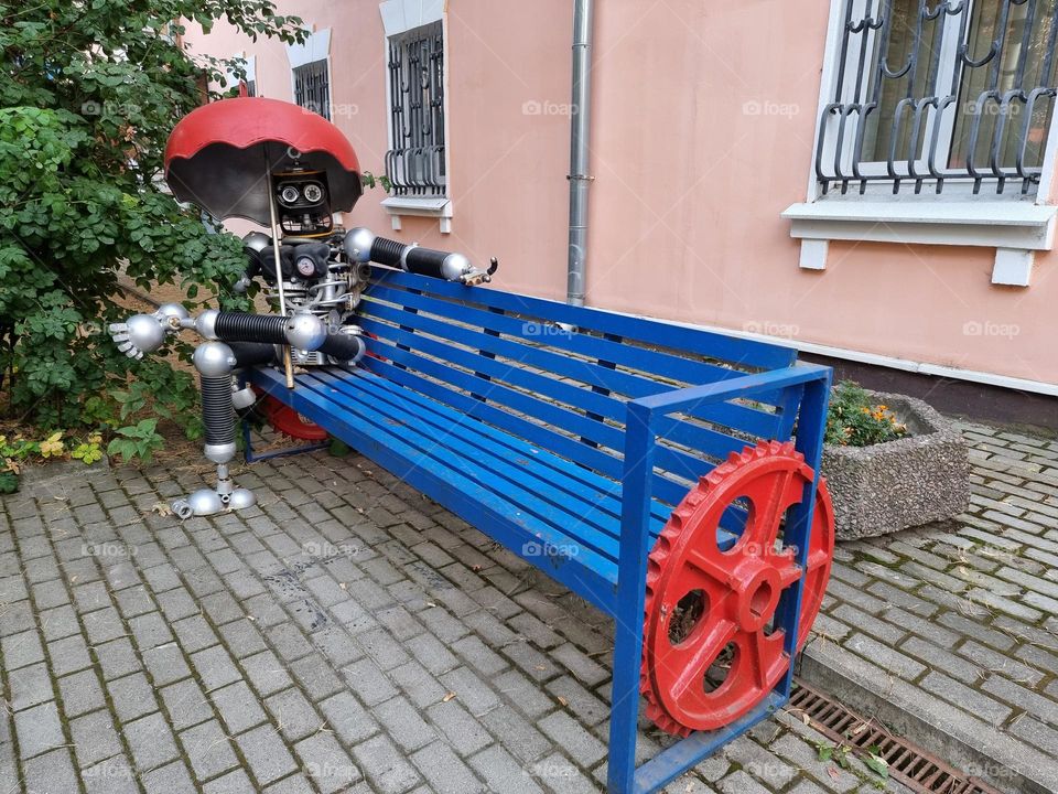 Robot-like figure sitting on a blue bench