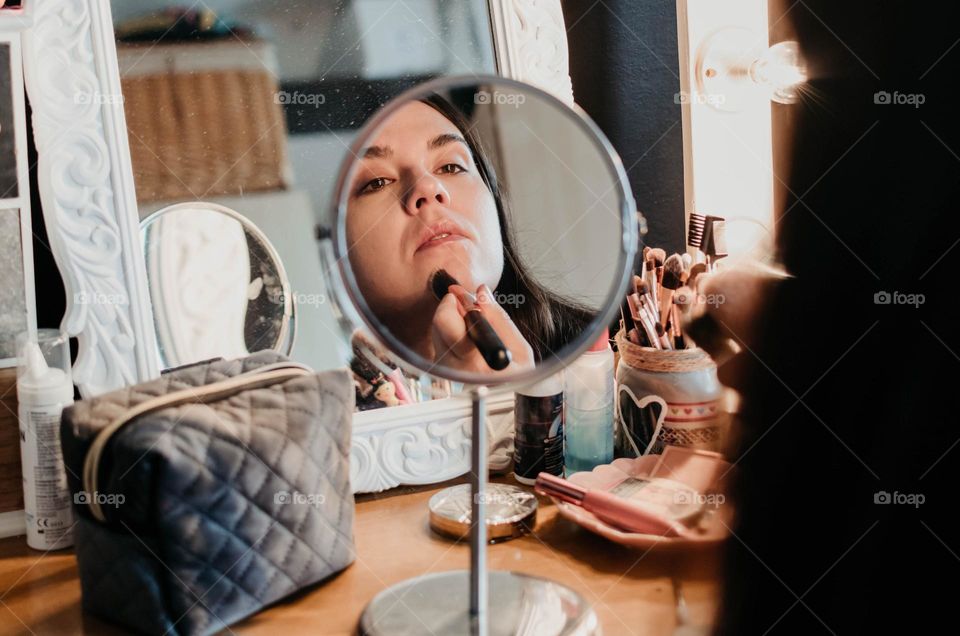 Close-up of a woman doing make-up in front of small mirror