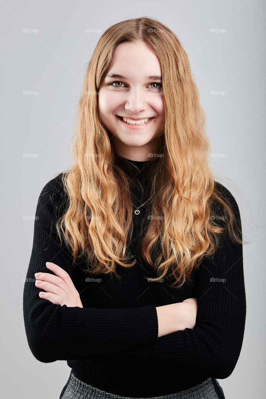 Portrait of pretty cheerful young woman holding arms crossed standing over a grey plain background