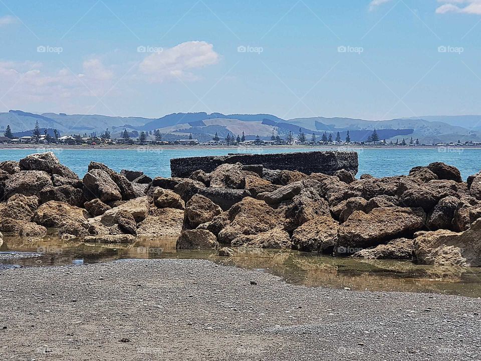 On the sea shore looking across to west shore in Napier. A big square concrete slab sits beyond the rocks. It is the remains of the bomb shelter from years gone by.