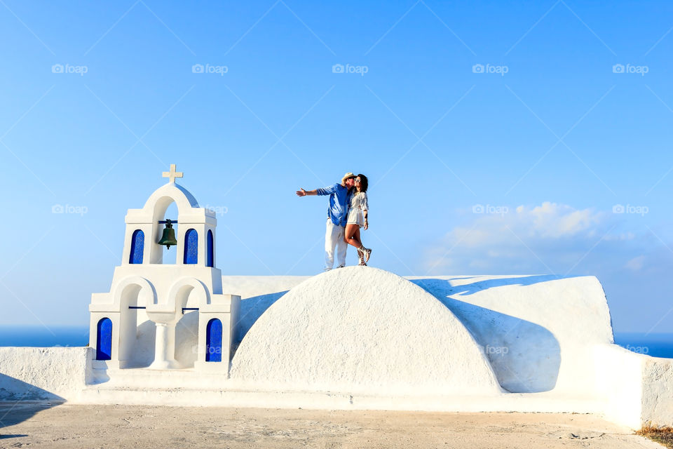 Couple enjoying city. Couple enjoying posing on chapel with beautiful blue sky on background in Santorini, Greece 