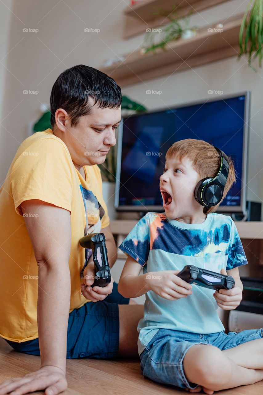 Father and son play video games at home. Parenthood, family time and fun. Modern technologies