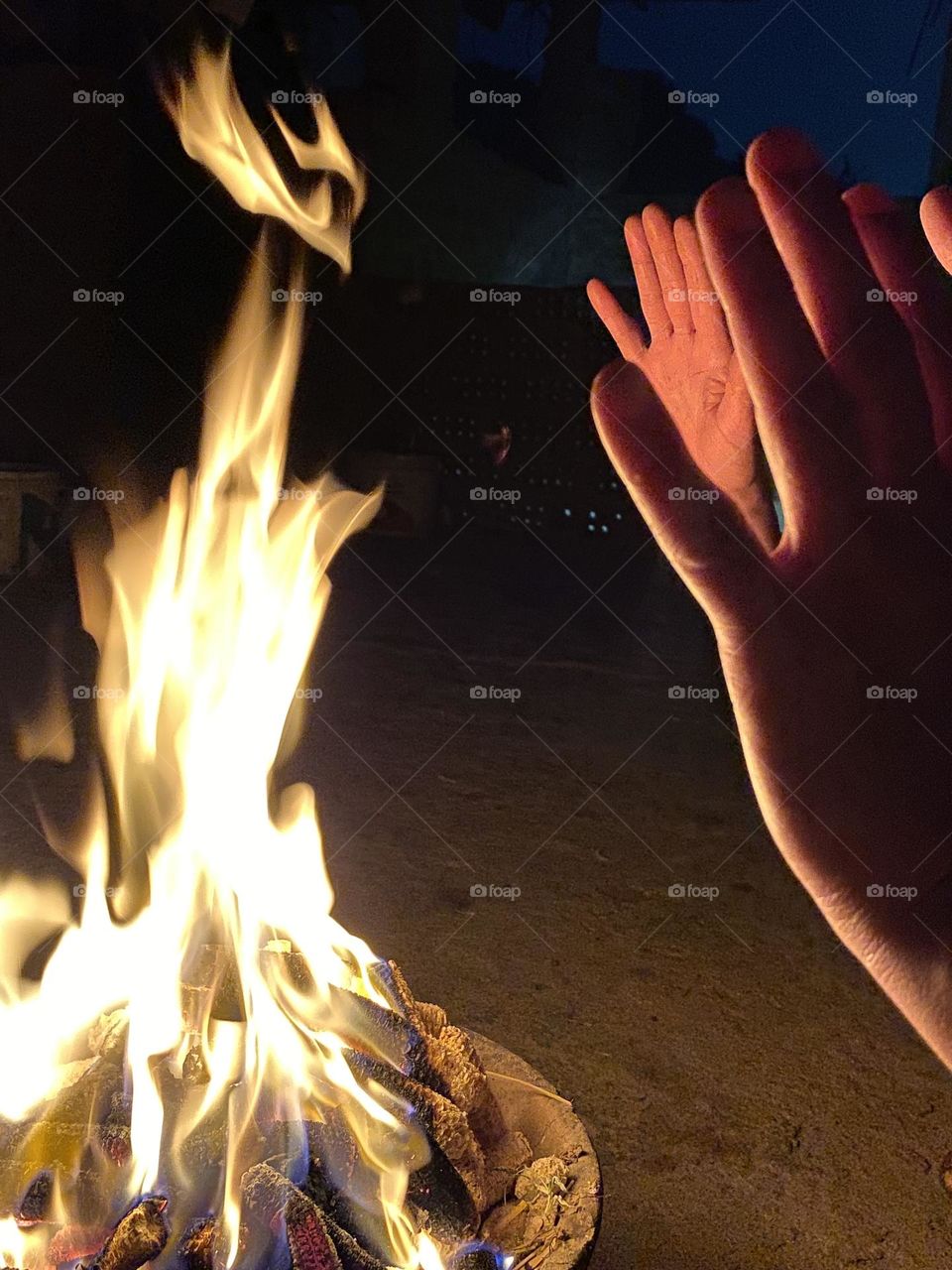 Some women are warming their hands next to a camp fire 