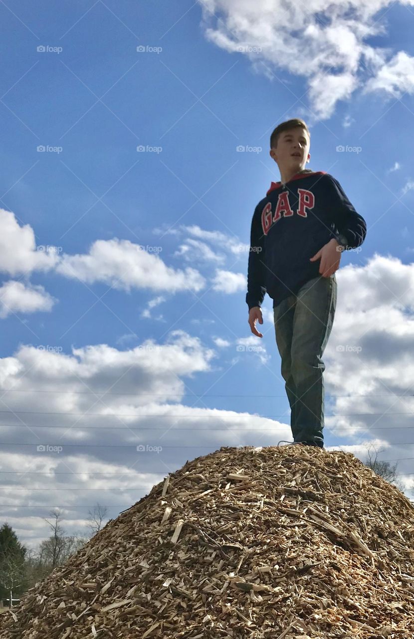 A boy standing on a pile of wood chips viewed from the ground up