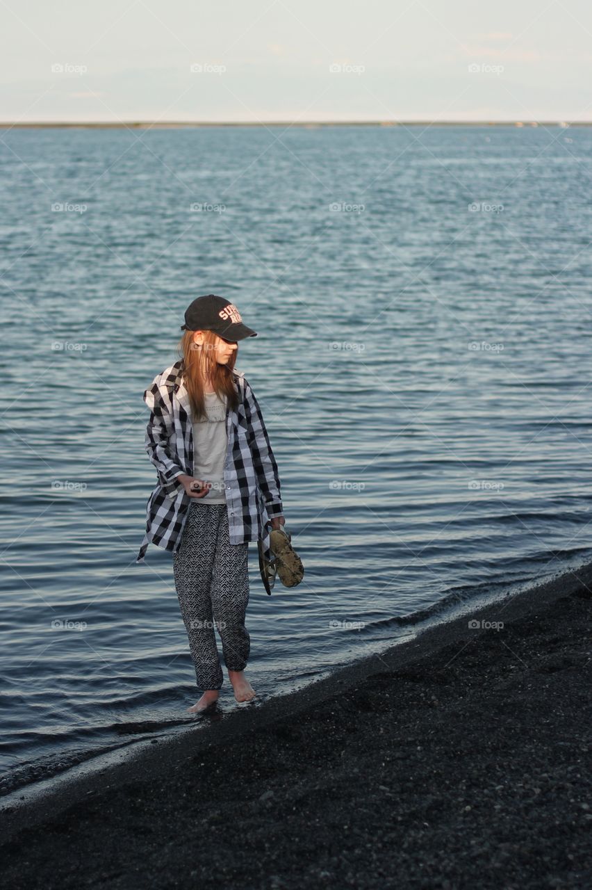 A girl walks along the beach barefoot and collects stones.