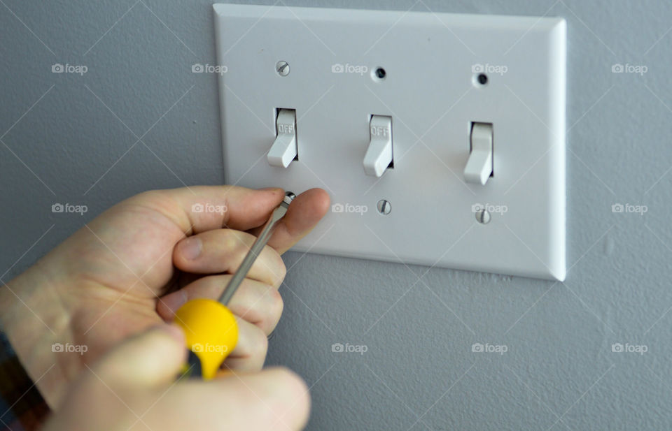 Close-up of handyman's hands screwing on a light switch plate