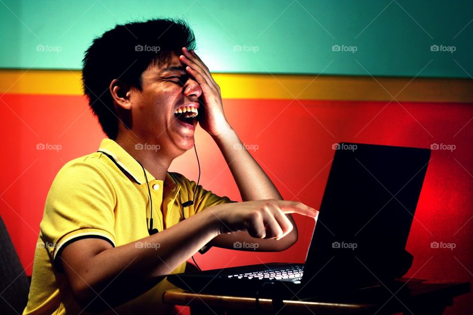 young asian teen working on a laptop computer and laughing