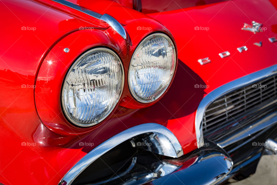 Closeup photo of the twin headlights of a classic Corvette in the sun with catch lights in the bright chrome trim