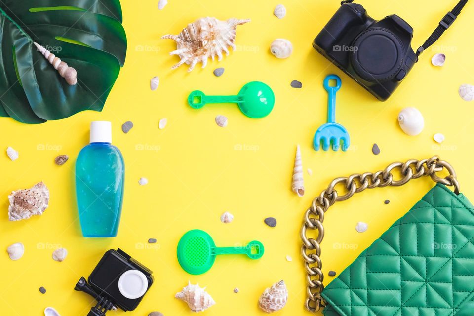 Women's fashionable quilted bag with a large chain, two cameras, one tube of after-sun cream, children's sand toys, shells and a manster leaf lie on a wall background, flat lay close-up.