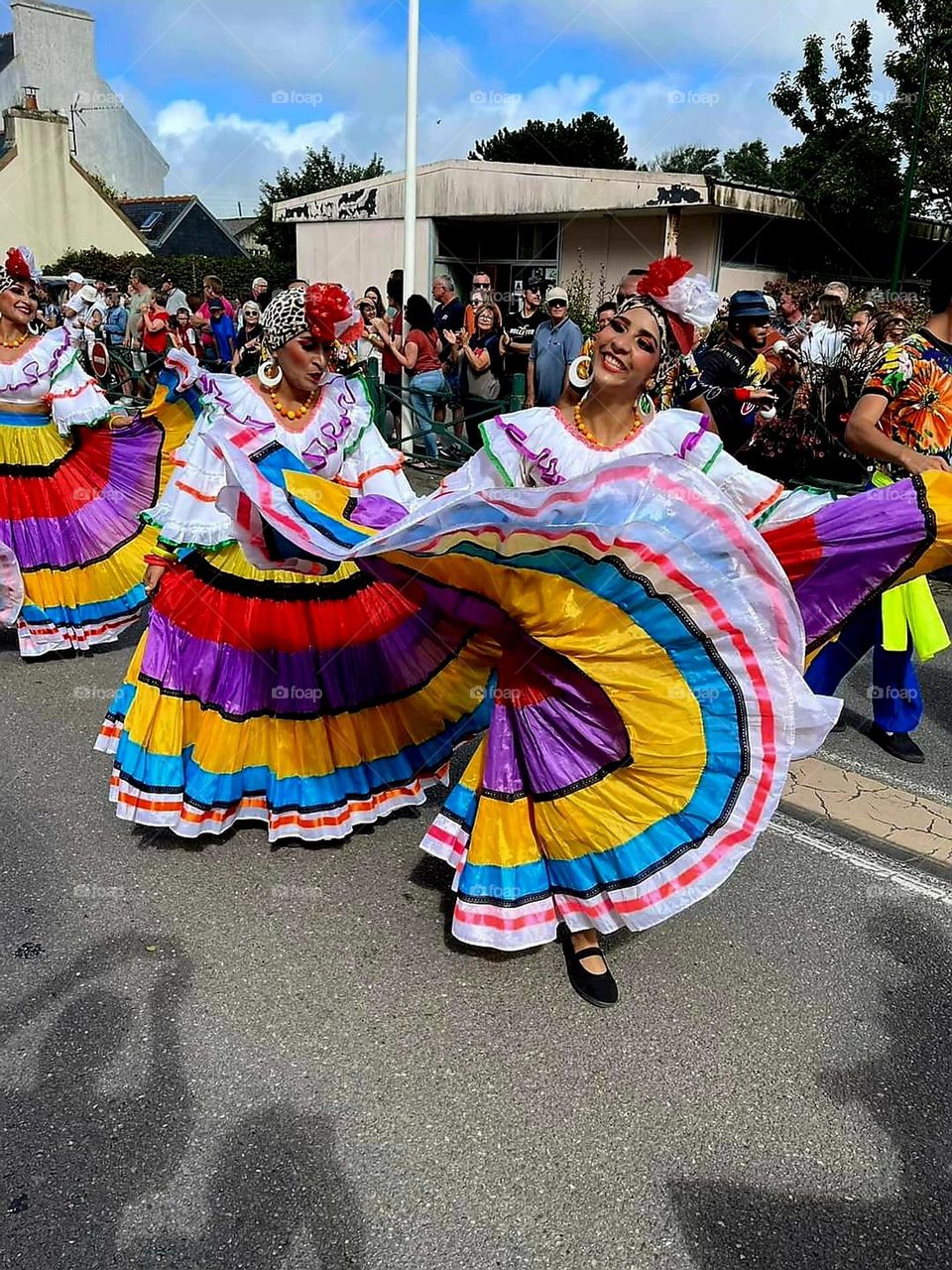 Smiling black women dressed in multi-coloured costumes dancing in a street of Plozevet at the World Folklore Festival