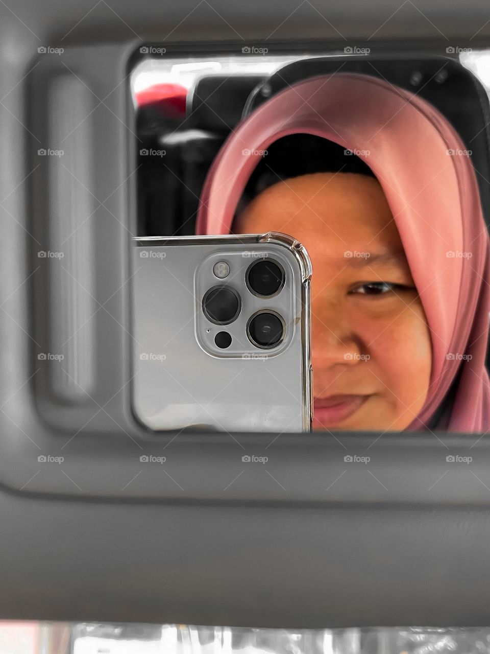 A woman with hijab reflection smiling while looking at the phone