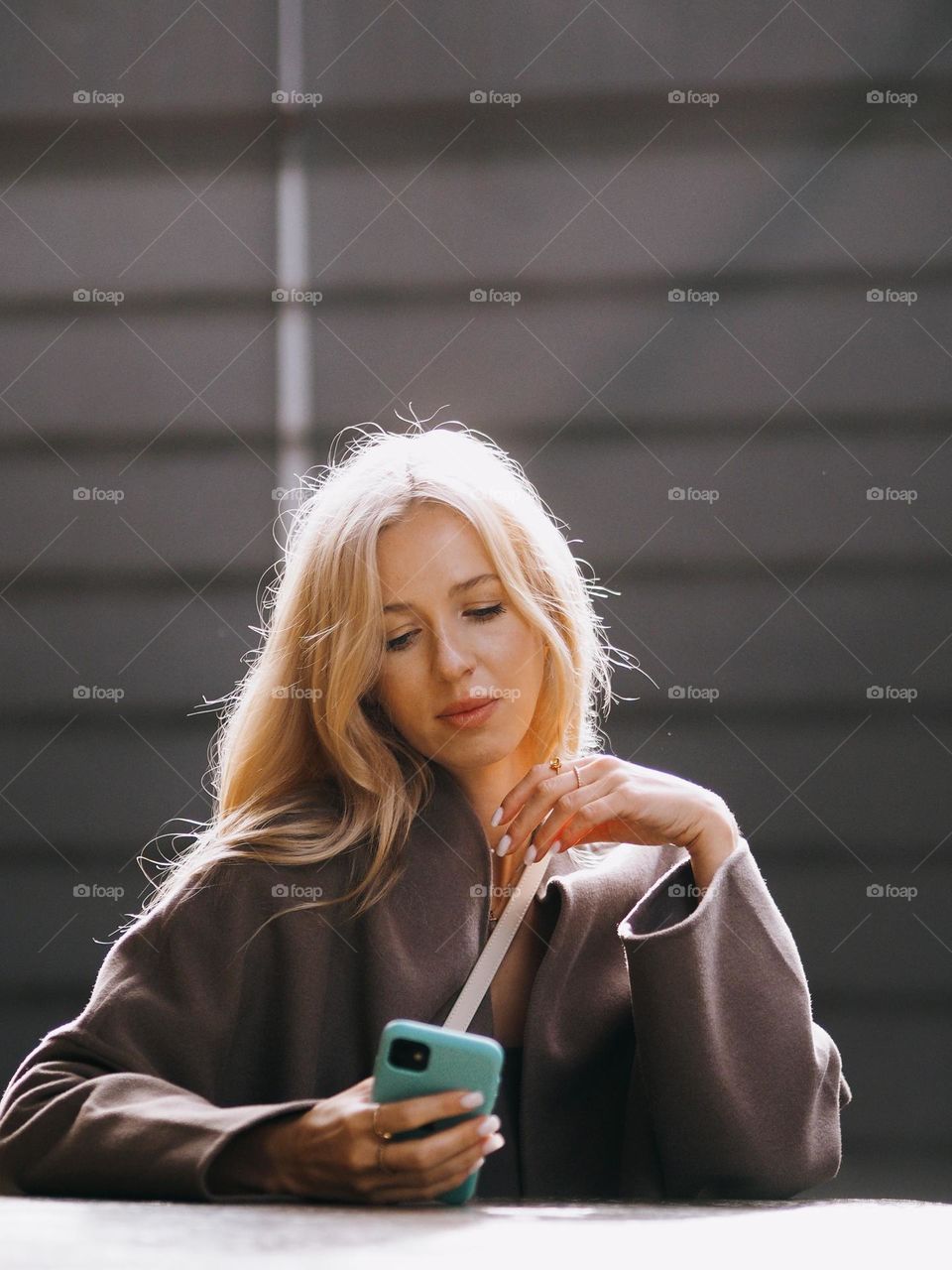 Young beautiful blonde woman sitting in modern cafe and using smartphone in sunny day, portrait of woman 