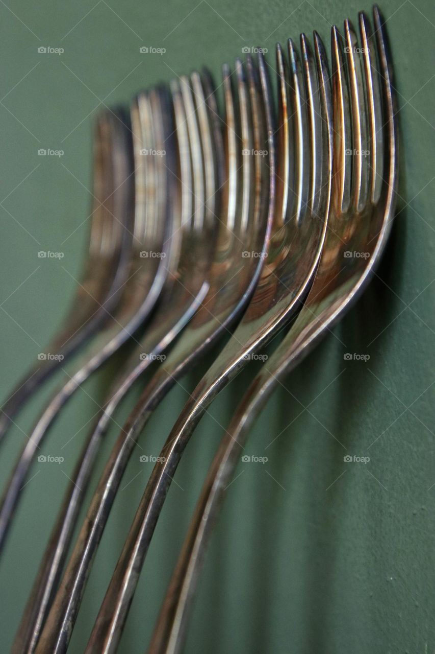 Close up of silver forks standing on green wall 