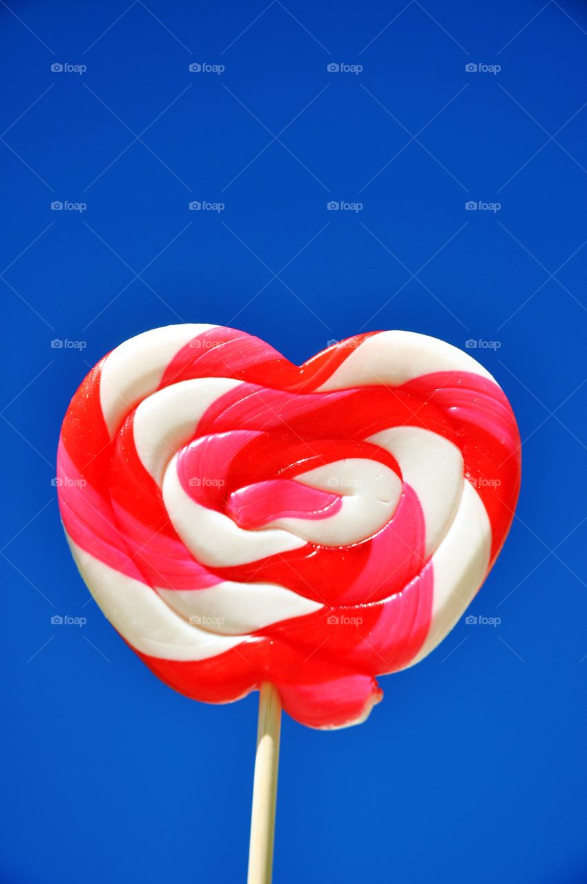 Heart shaped lollipop against a bright blue sky. 