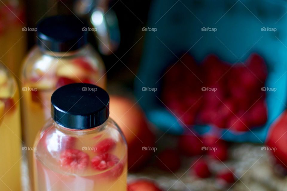Closeup of kombucha, bottled for a second-ferment and flavored with nectarines, raspberries and slices of ginger root, whole nectarines and raspberries in a paper carton in the background