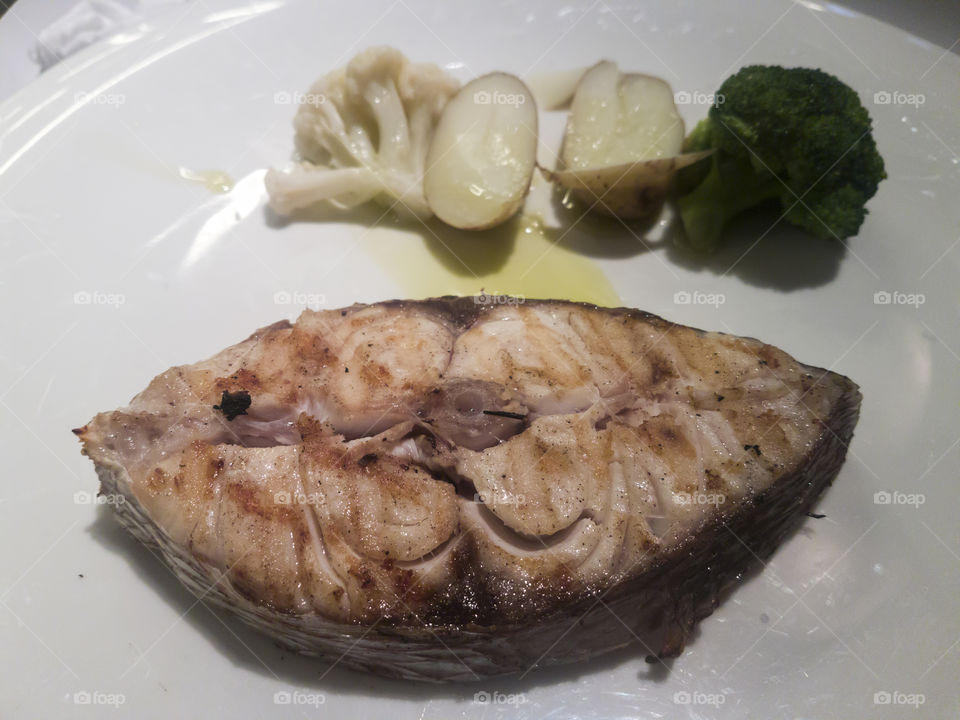 Slice of cooked sea bream fish served on a plate with vegetables.