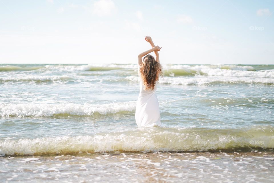 Young beautiful woman with long hair in white dress enjoying life on sea beach on sunset