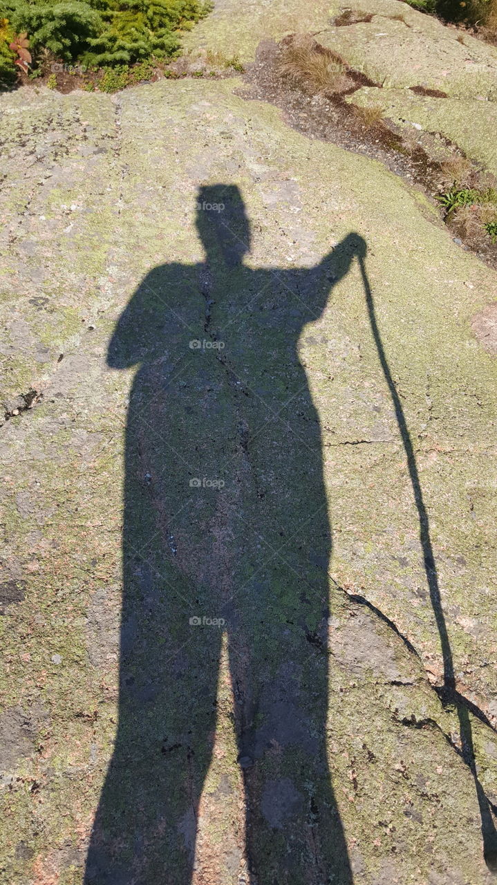 A hiker marks their shadow as the sun passes over them and over the top of the mountain.