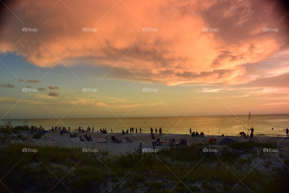 A crowded beach in Tampa bay, Florida watches a beautiful sunset and skyline.
