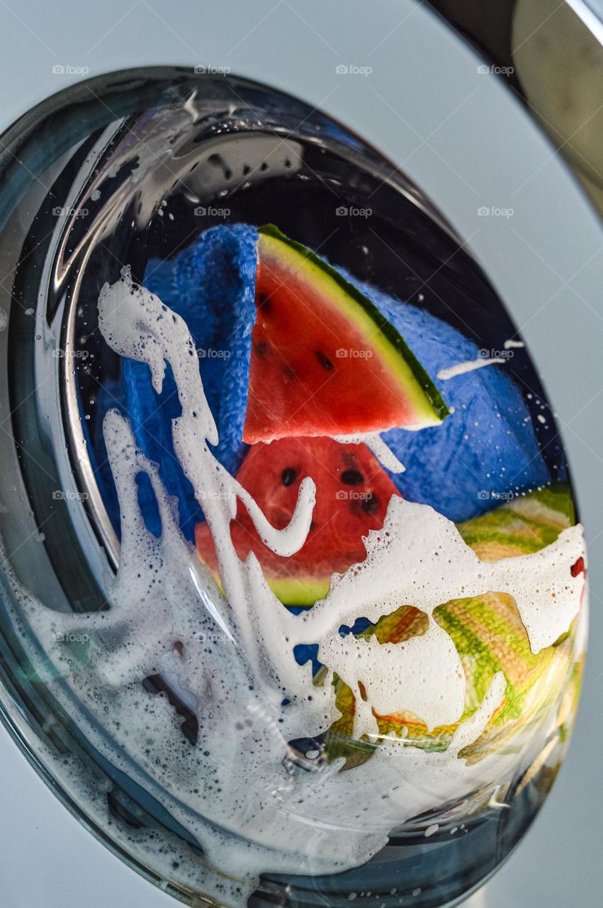 Pieces of watermelon in the washing machine drum spin in the foam with the laundry