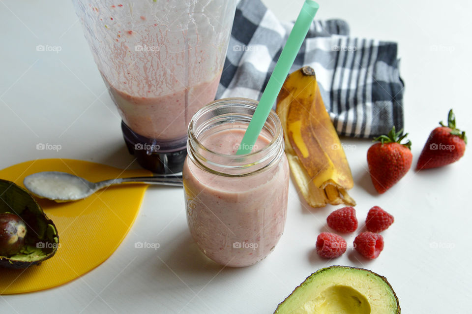 Fresh fruit smoothie in a glass with banana peel, raspberries, strawberries, and avocado