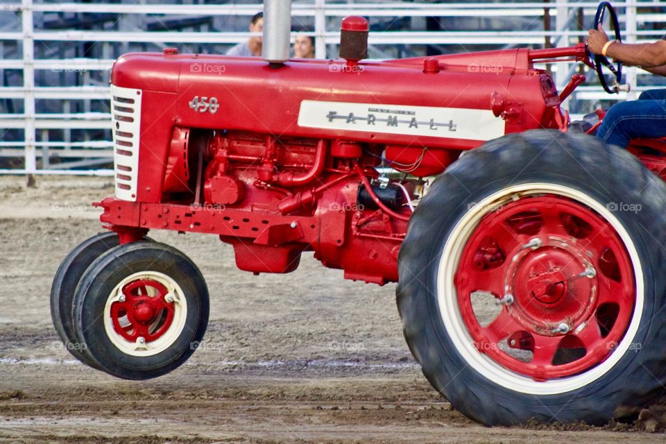 Isolated view of an antique International Farmall 450 tractor with front wheels off of the ground as its driver tries to get traction on a dirt track during a tractor pull