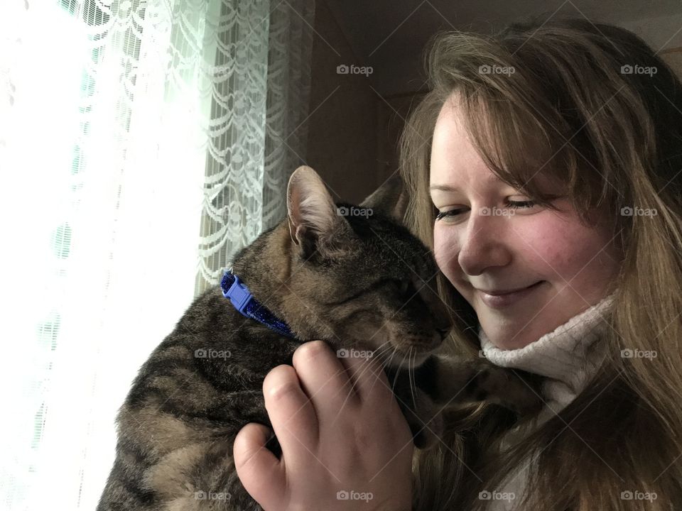 The girl is smiling and cuddling a cat.
