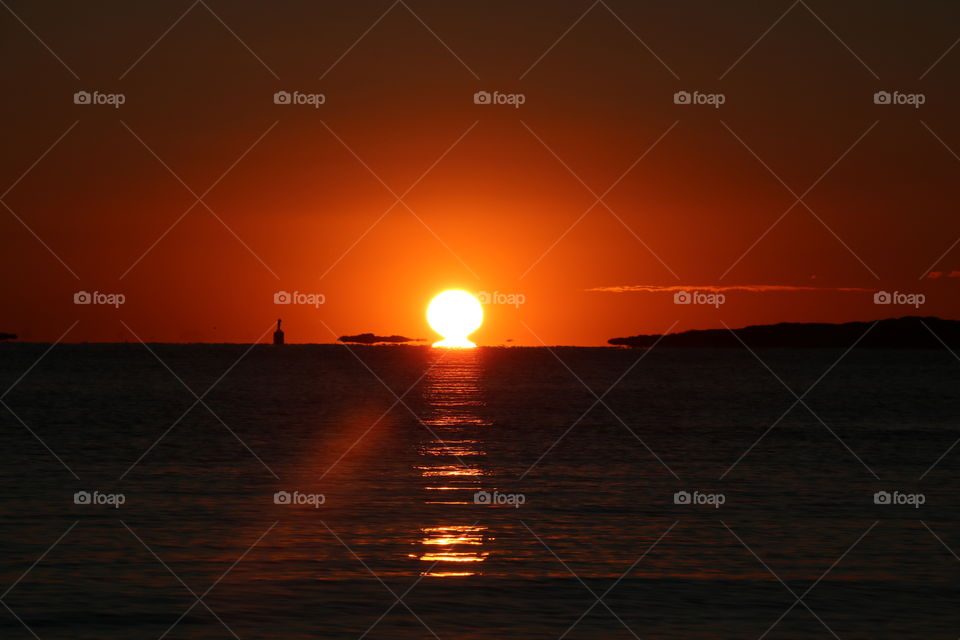 Sun rises above the horizon mirroring itself into the ocean... sky red and no clouds on this winter morning 