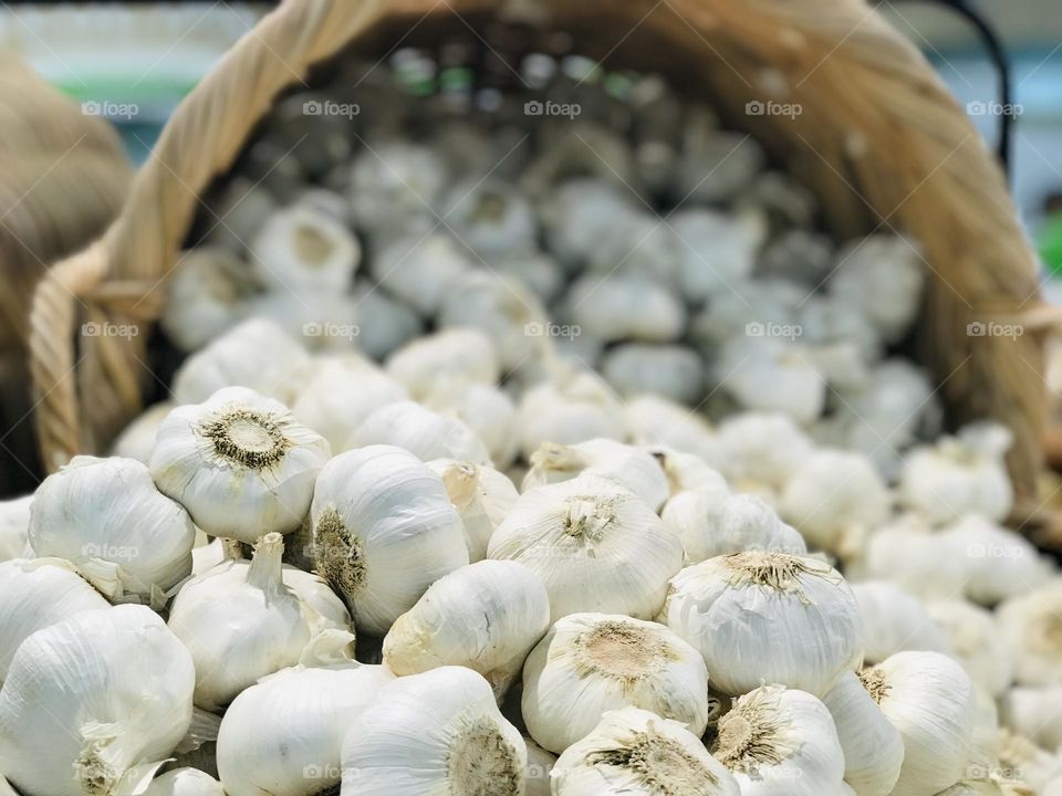 A flatten bamboo basket full of garlic.