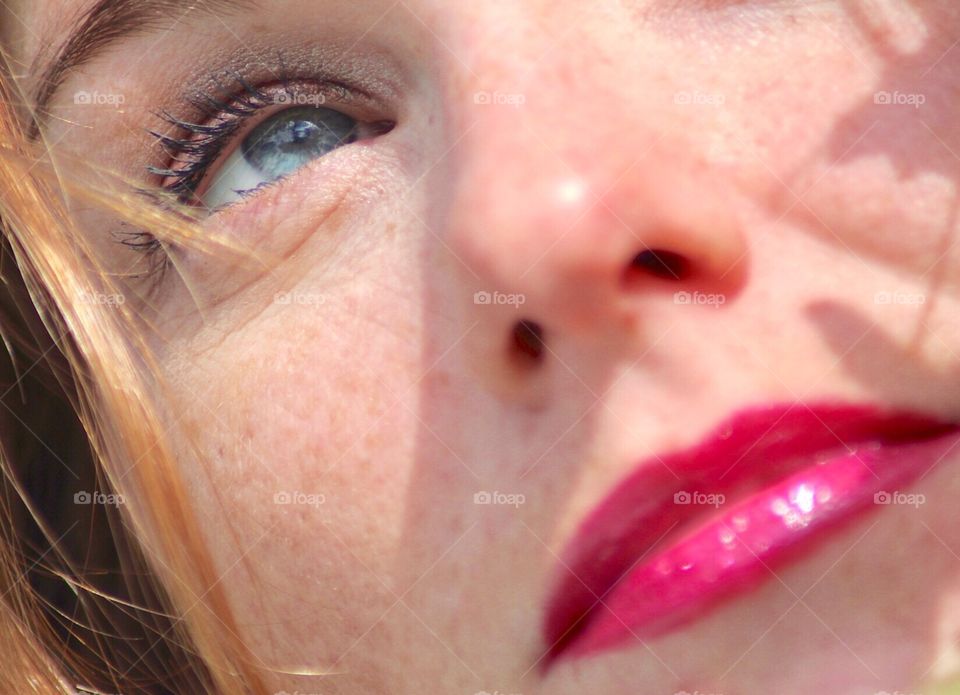 Reflective gaze of a young redheaded woman with blue eyes and pink lips. Shadows of foliage lay gently across her pale cheek!