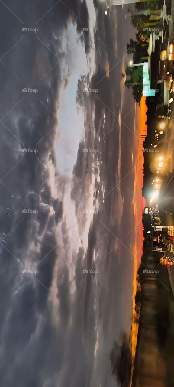 The dramatic interplay between the natural beauty of the sunset and the urban lights creates a captivating scene, evoking a sense of tranquility and wonder as day transitions into night.