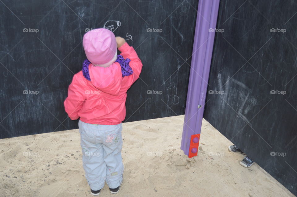 small girl draws a chalk on the board at the playground